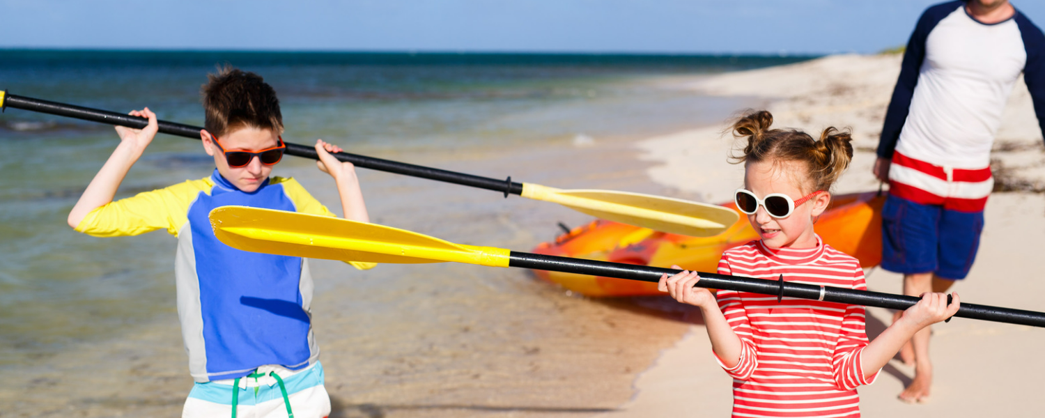 Two kids and dad on beach kayaking.