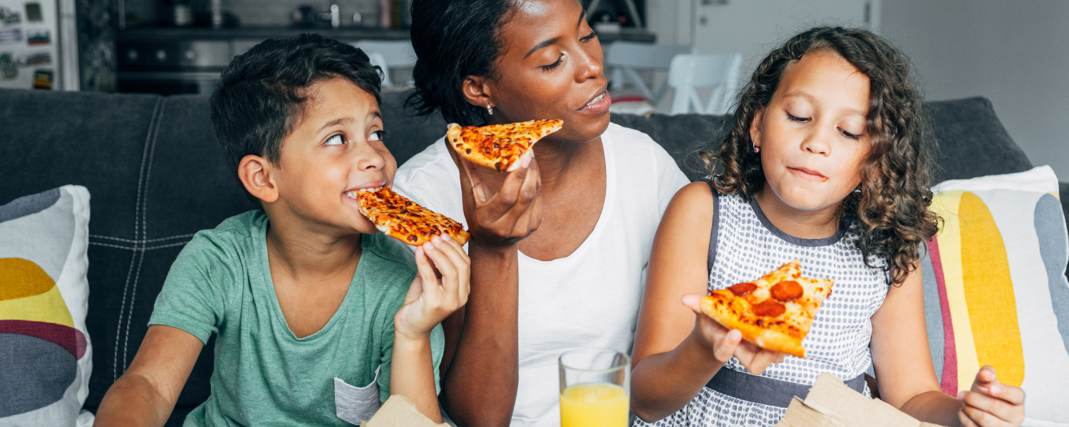 african american mother and two children eating pizza on couch